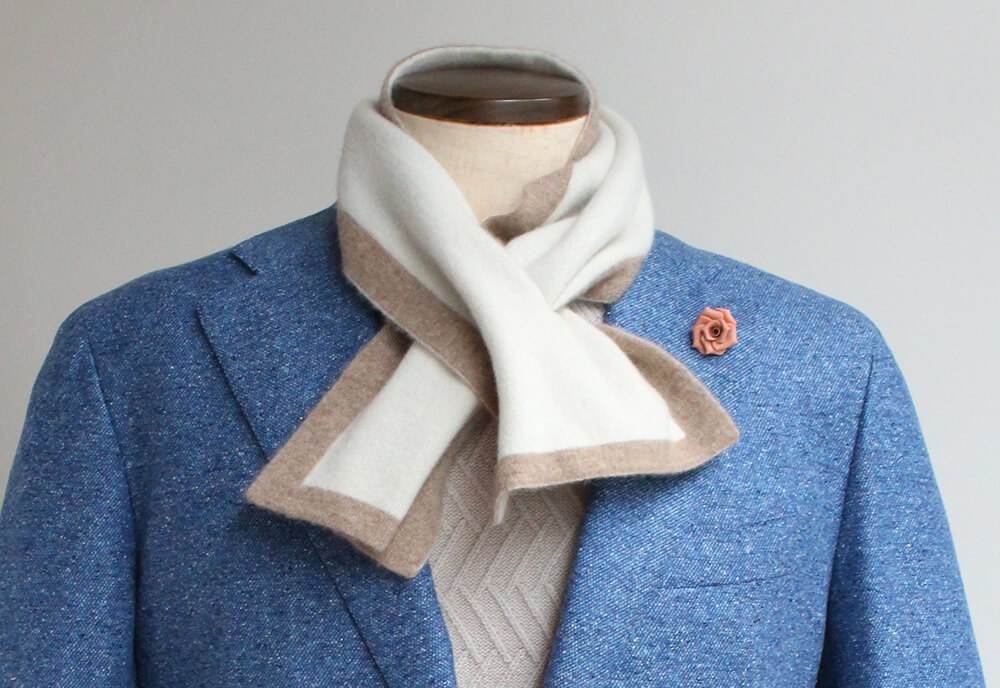 ウィリアムロッキーのミニマフラーを使ったコーディネート写真。明るいブルーのジャケットにアイボリーとモカベージュのバイカラーのマフラーを合わせている