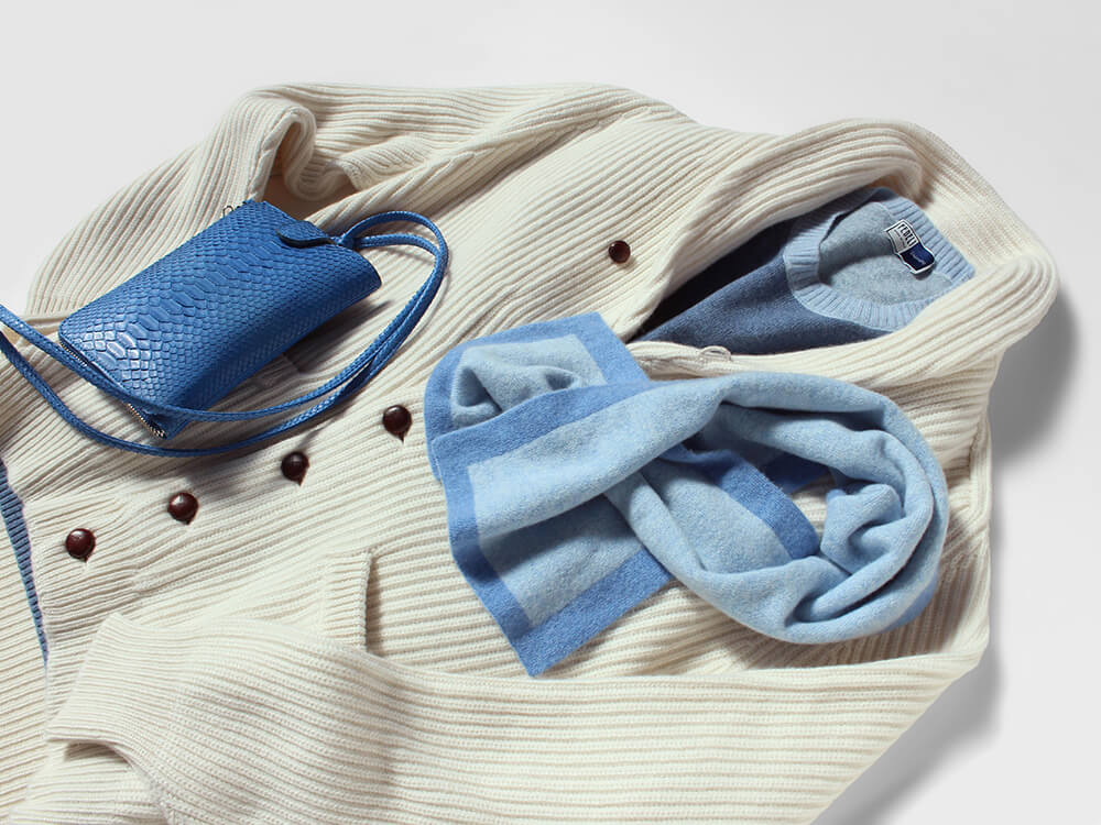 ウィリアムロッキーのミニマフラーを使ったコーディネート写真。明るいアイボリーのニットジャケットにサックスブルーとブルーのバイカラーマフラーを合わせている